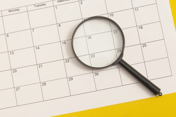 Magnifying glass on white clean calendar on solid yellow background